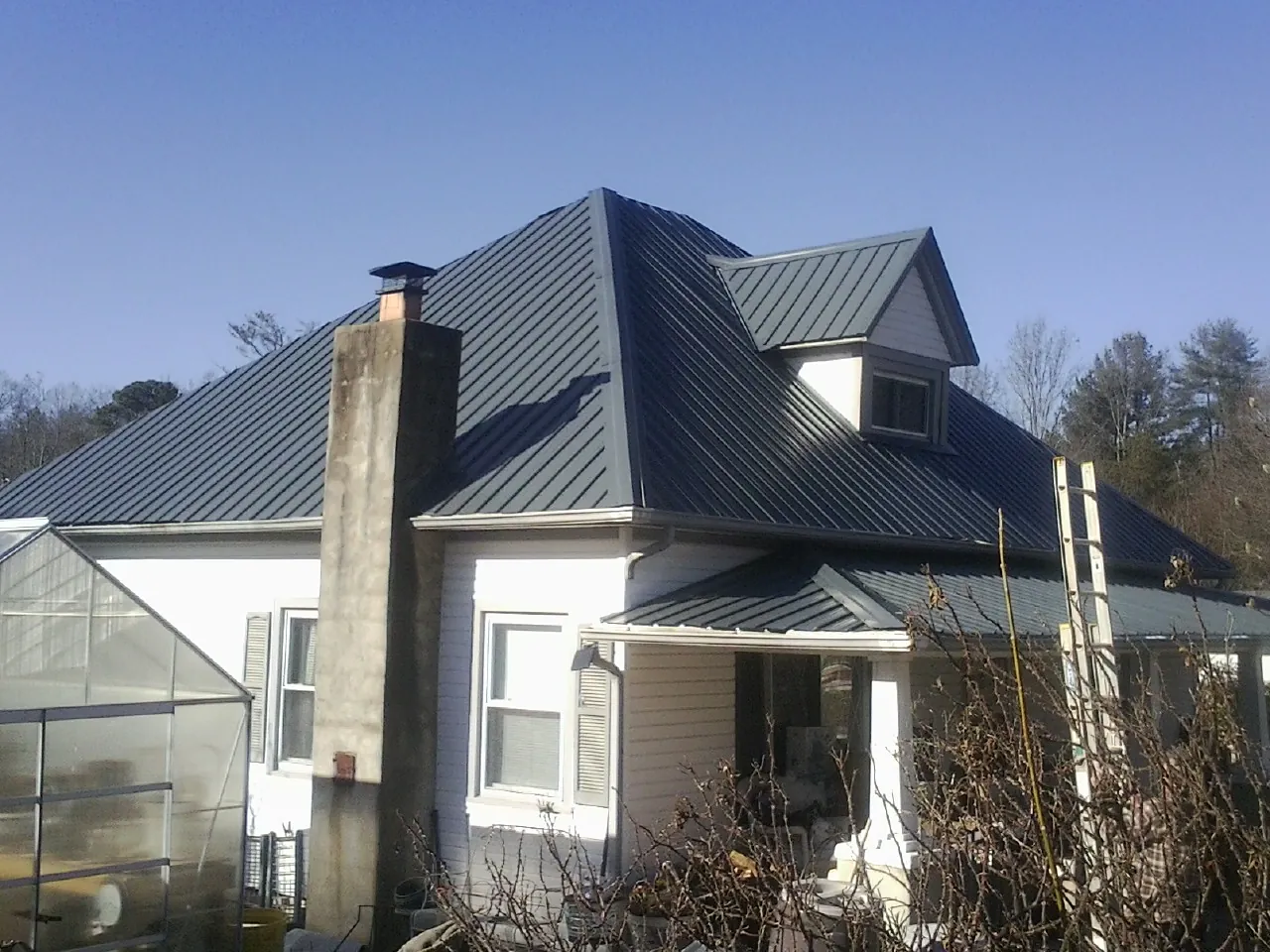 Dark blue standing seam metal roof on a white farmhouse with dormer — Slate & Tile Roof Repair by Roofing Brothers in Vilas