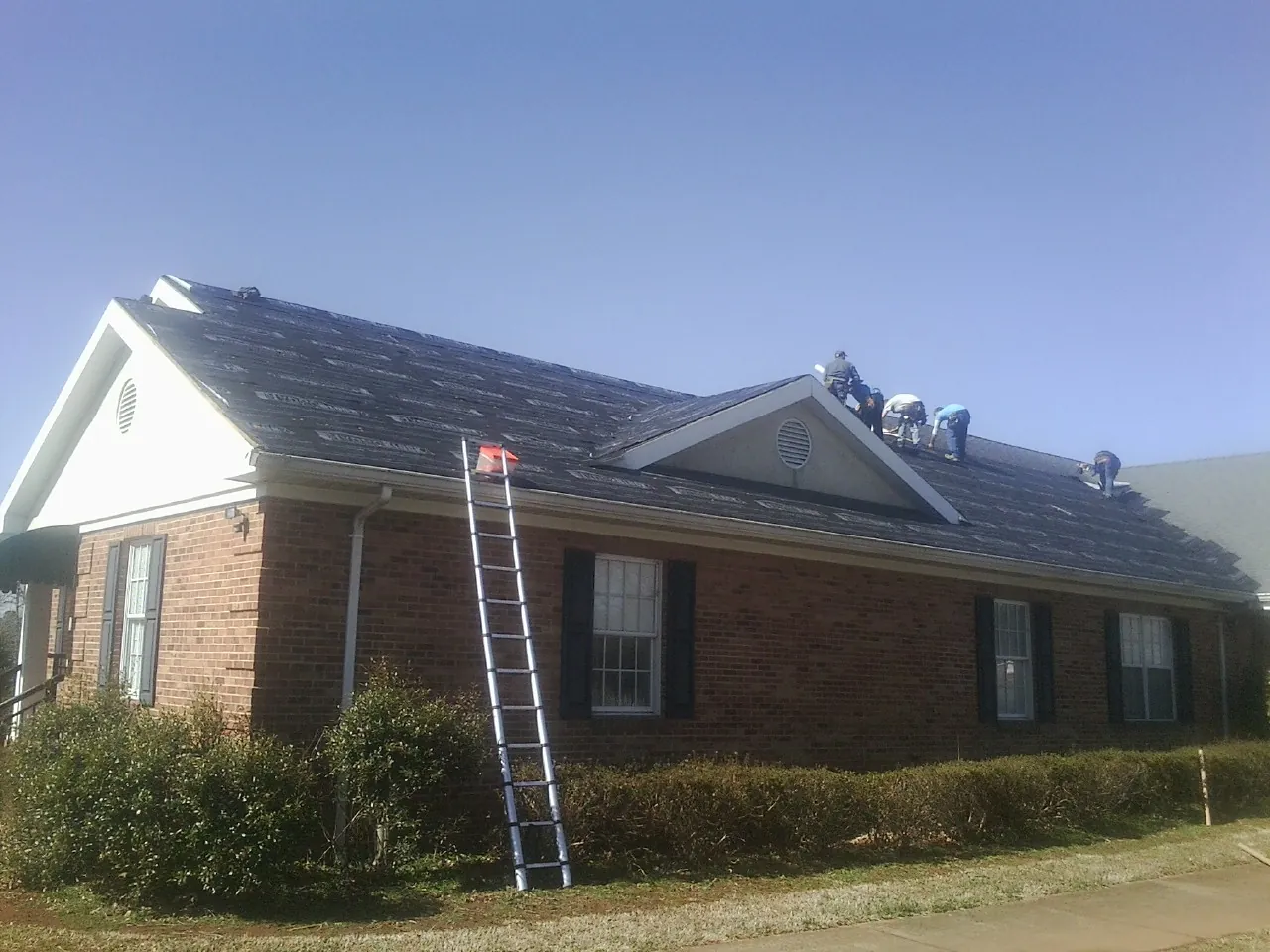 Crew tearing shingles off a brick ranch roof with a ladder set — Emergency Roof Repair work by our crew in Vilas