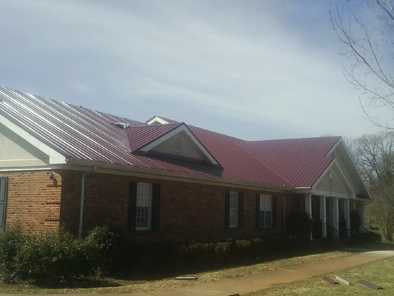 Red metal roof with gabled entries on a long brick building, from a Hail Damage Roof Repair job in Vilas