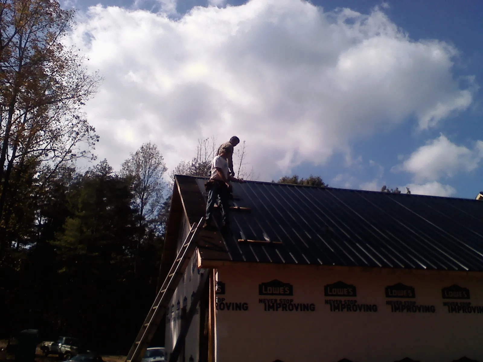 Roofer fastening dark metal panels high against a cloudy sky, from a Roof Inspection job in Vilas